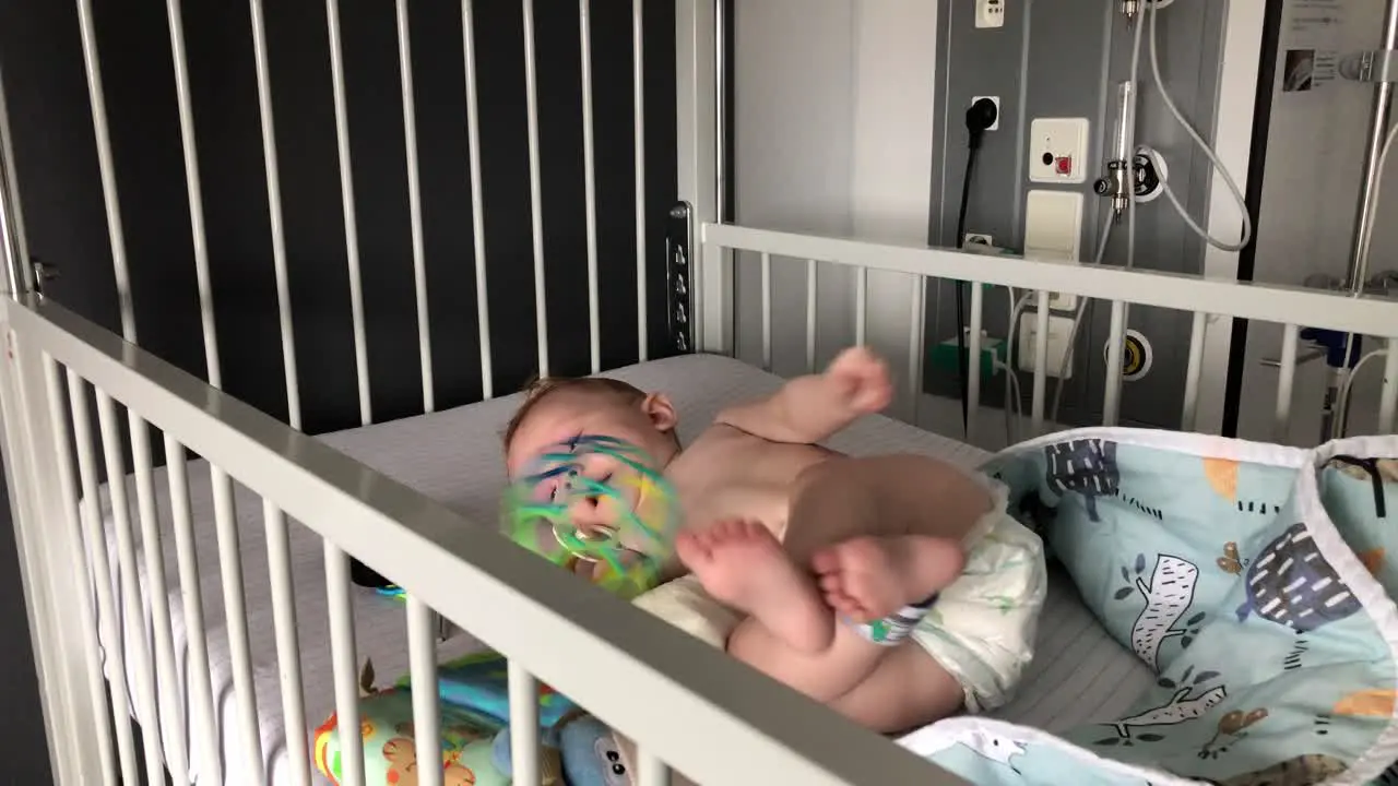 Baby trying to roll over and playing with her colourful ball in the hospital