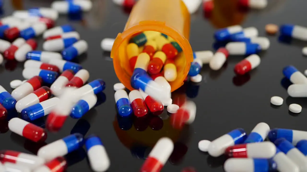 Many prescription pills drugs and antibiotics falling in slow motion on an orange pharmacy medicine bottle