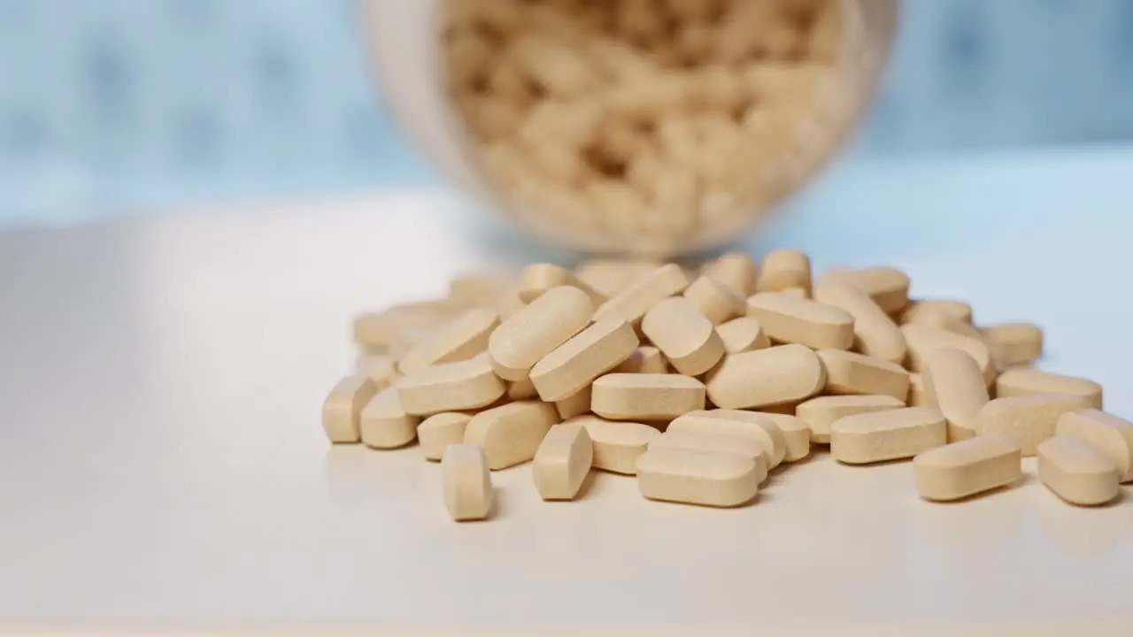 Vitamin C tablets poured out of bottle onto table close up slow motion