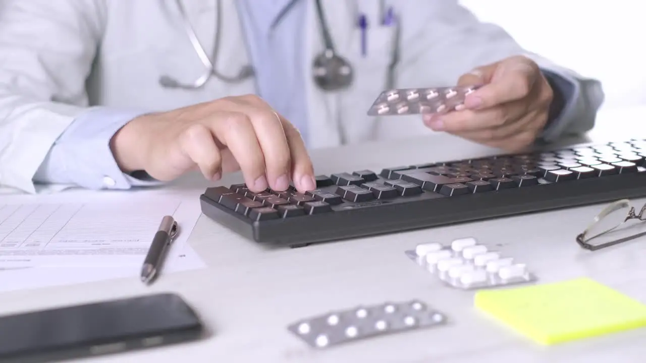 Doctor Typing on computer keyboard holding a medicine pills Nutrition appointment Close-up Shot