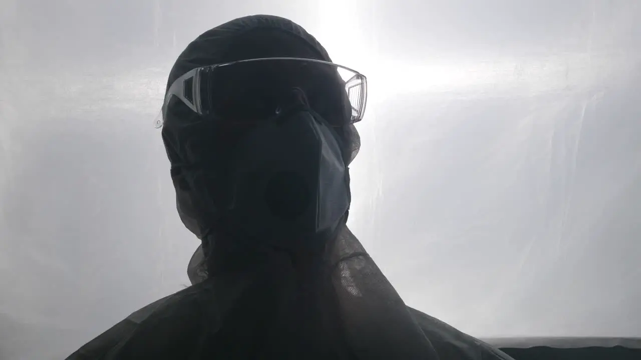 Lab worker in medical protective suit face mask and goggles nervously looks around laboratory