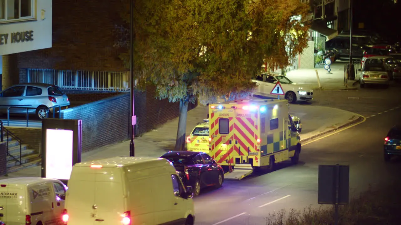 London ambulance with flashing lights parked on a street at night in traffic