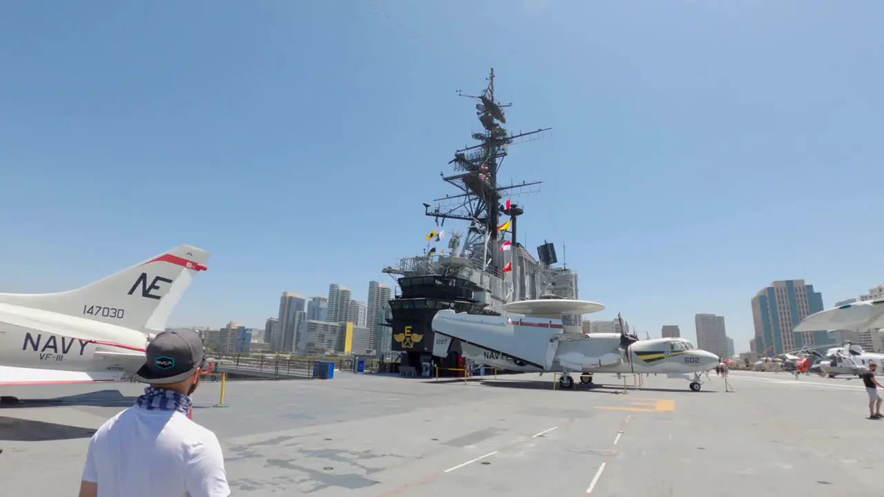 Tourists walking on flight deck of the USS Midway Museum with downtown cityscape in background