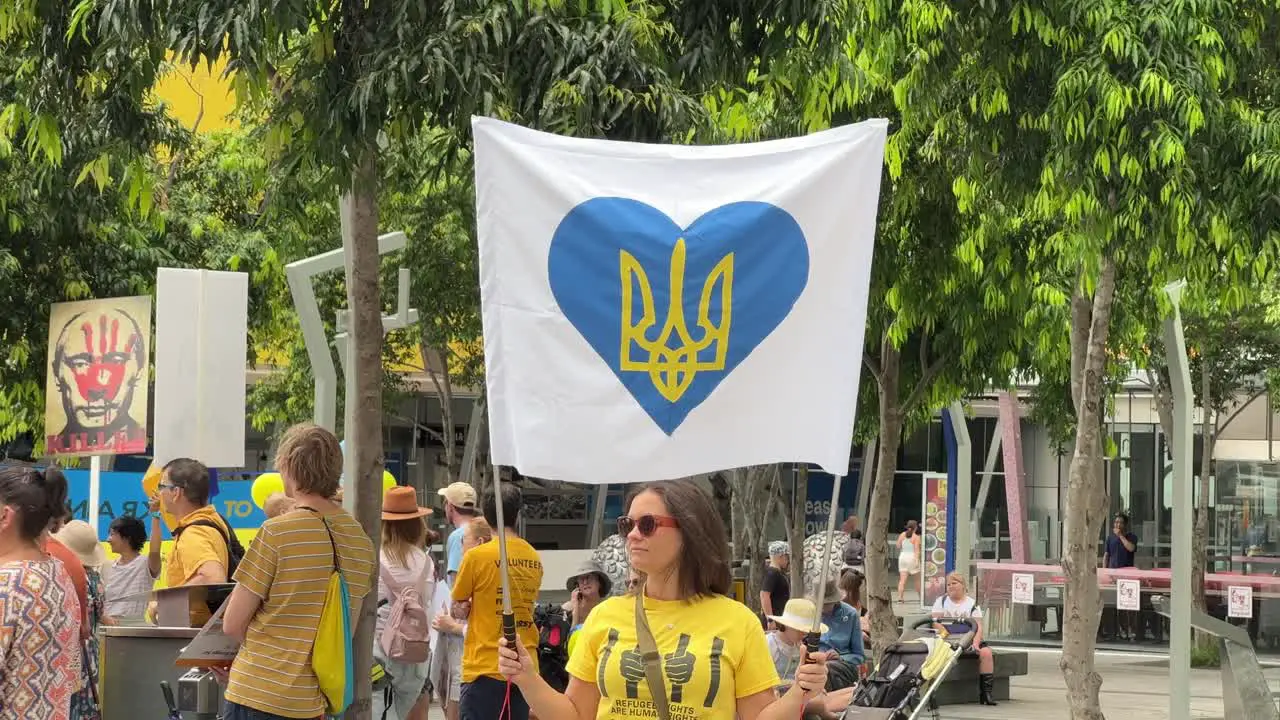 Peace loving pacifist woman at Brisbane Square holding up banner with heart shape coat of arms of Ukraine during the demonstration calling for peace as tension between Russian and Ukraine rises