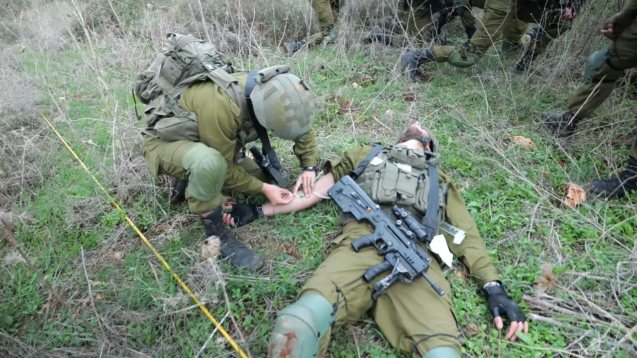 Israeli Army Medic Giving First Aid Injecting Needle into Vein of Wounded on Battlefield Soldier