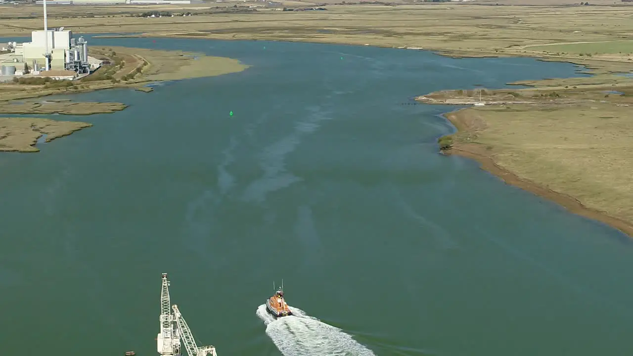 Aerial tracking shot of a RNLI Lifeboat crew sailing down the Swale Estuary between Ridham Dock at Kemsely and the Isle Of Sheppey