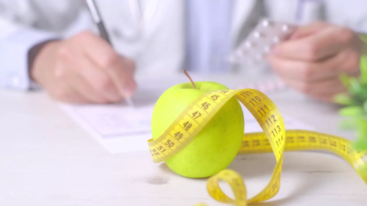 Nutrition appointment concept Doctor holding medicine blister an apple and measure tape in foreground