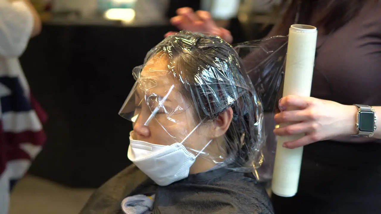 Hairdresser put on plastic wrap on Asian woman hair at the beauty salon during a covid-19 pandemic