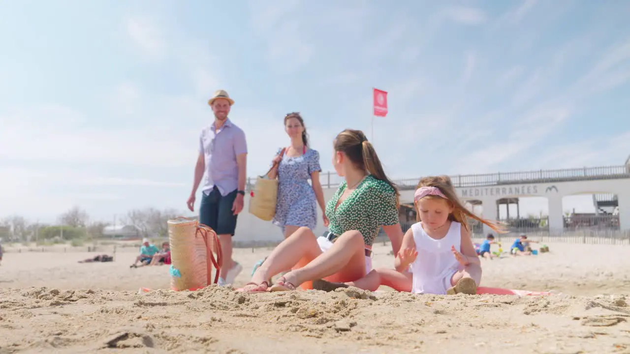 Mother and daughter sitting on the beach while mom welcomes her friends that just arrived