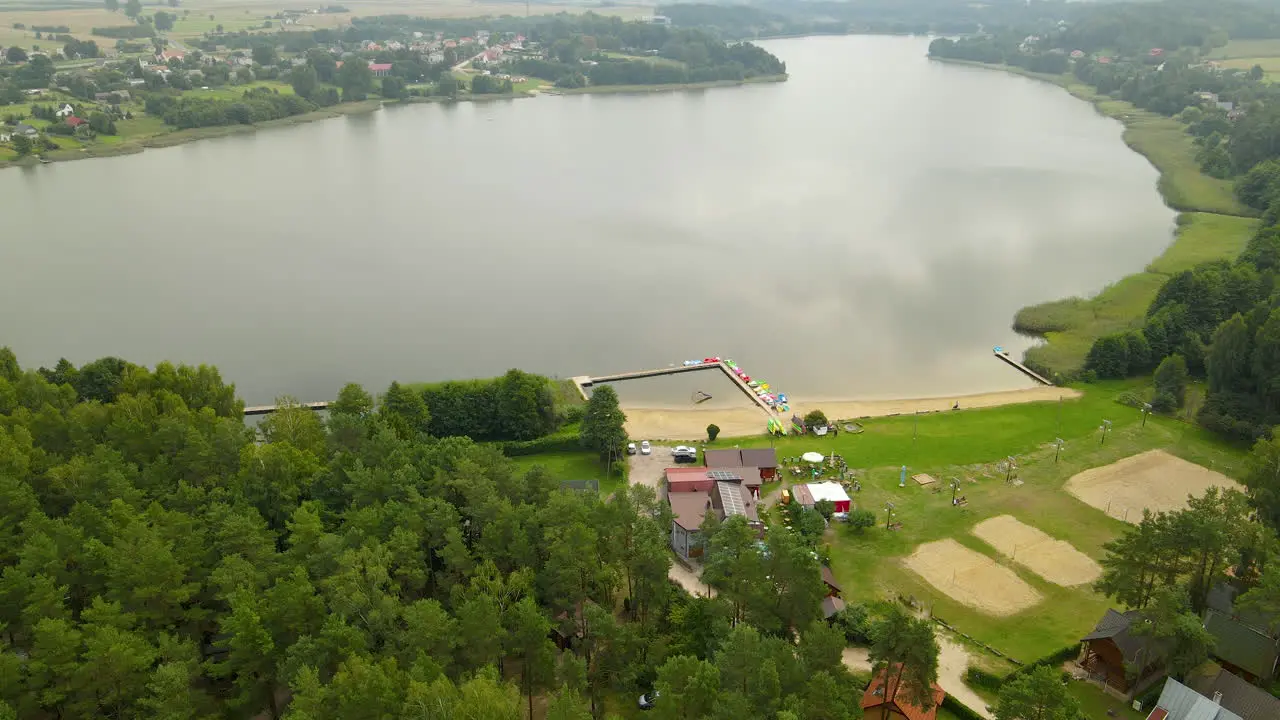 Aerial tilt down from Hartowiec lake landscape to Private Hotels equipped for summer water sports like kayaking canoeing pedal boarding and fishing surrounded by green dense forest Poland