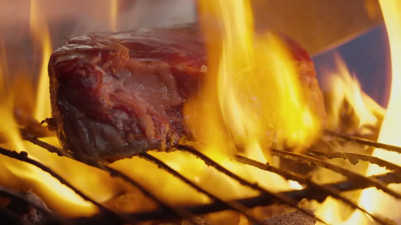 A cook turns a grilled steak amid flames smoke and barbecue coals