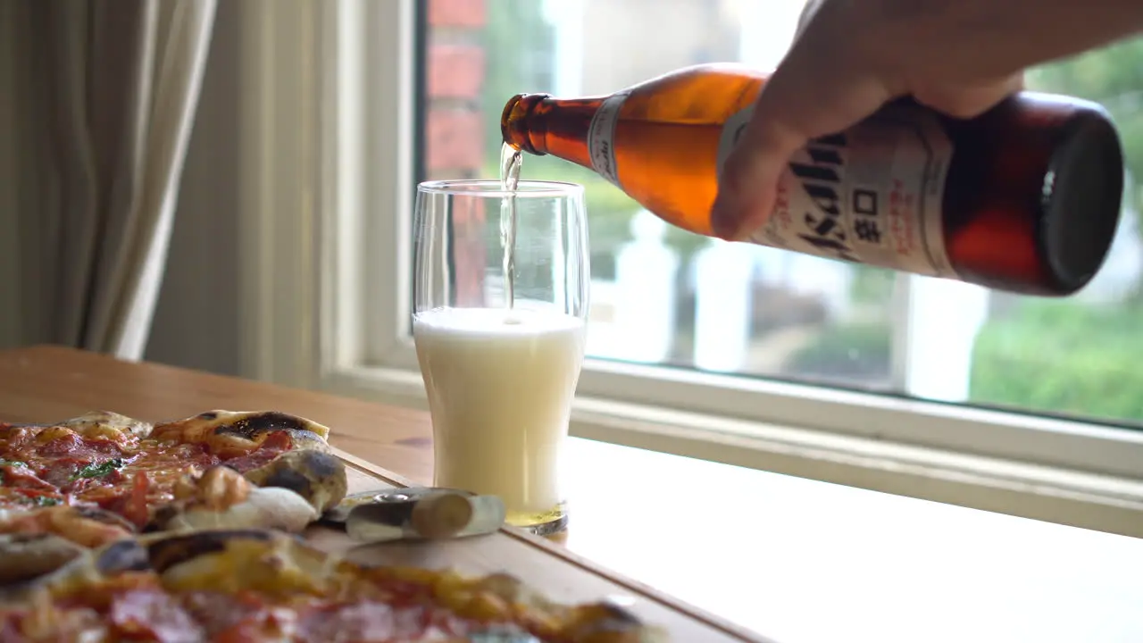 Man Pouring Asahi Beer in a glass while eating pizza