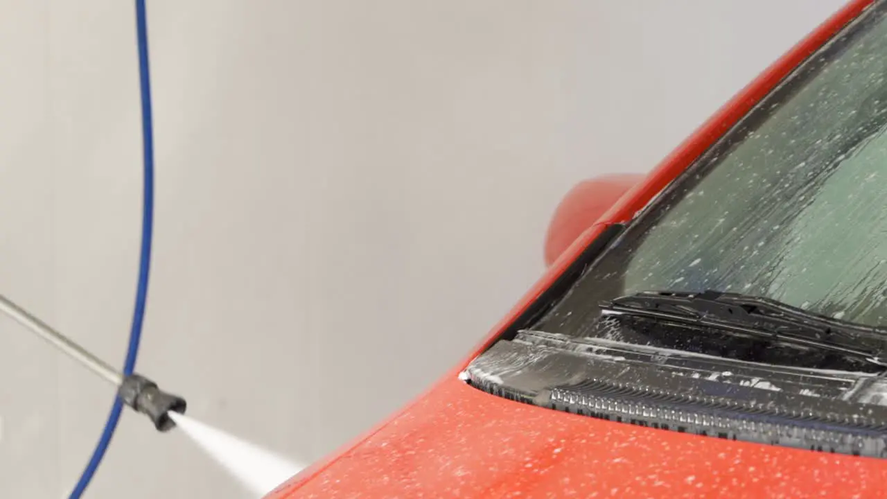 Pressure hose cleaning red car in car wash