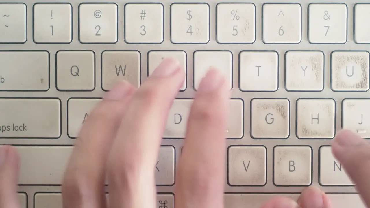 Medium shot of hands typing on a worn Mac Keyboard