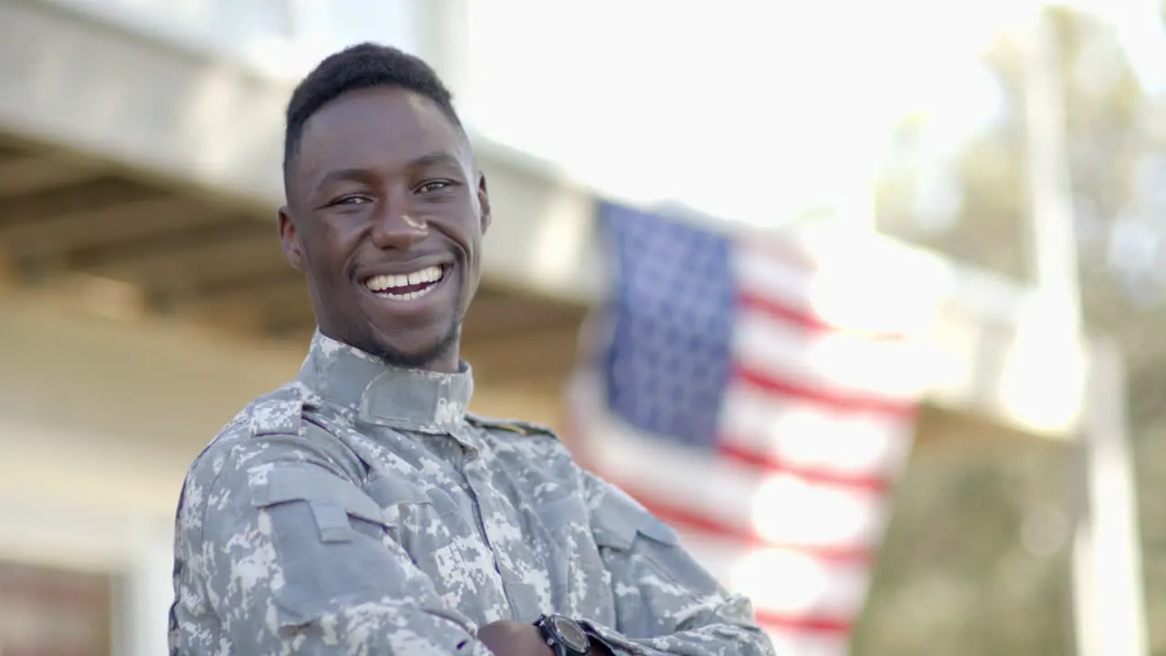 Happy african american male soldier laughing with flag in background on sunny day slow motion