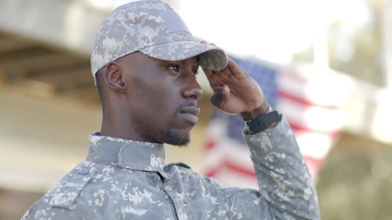 Serious african american male soldier saluting with flag in background on sunny day slow motion