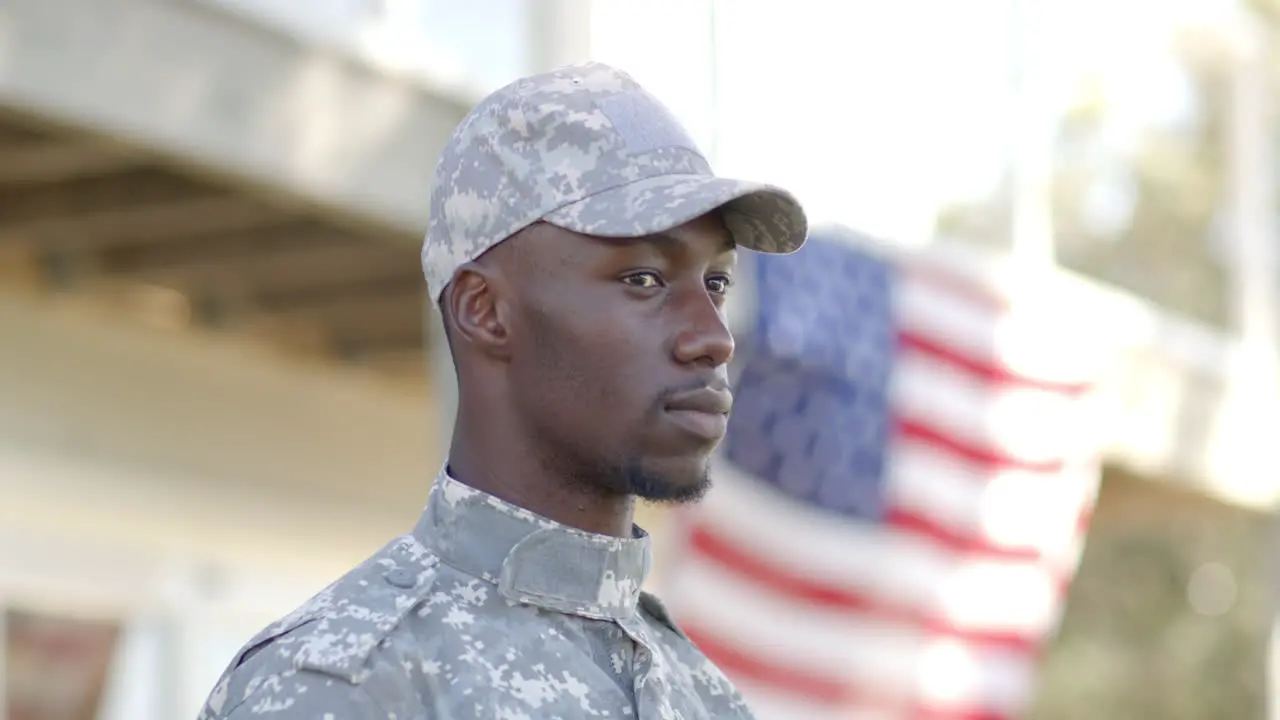 Serious african american male soldier standing with flag in background on sunny day slow motion