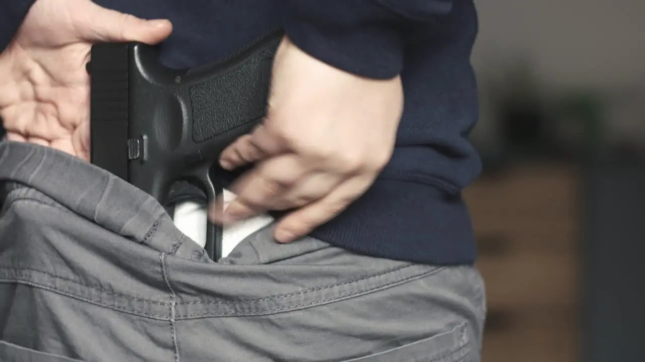 Close up of a young boy placing a nine millimeter toy gun perfect replica on the back of his pants and then hiding it under his sweatshirt