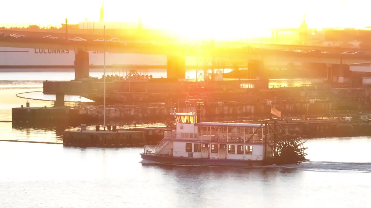 Paddle steamer boat on river at sunrise with naval ship and industrial backdrop