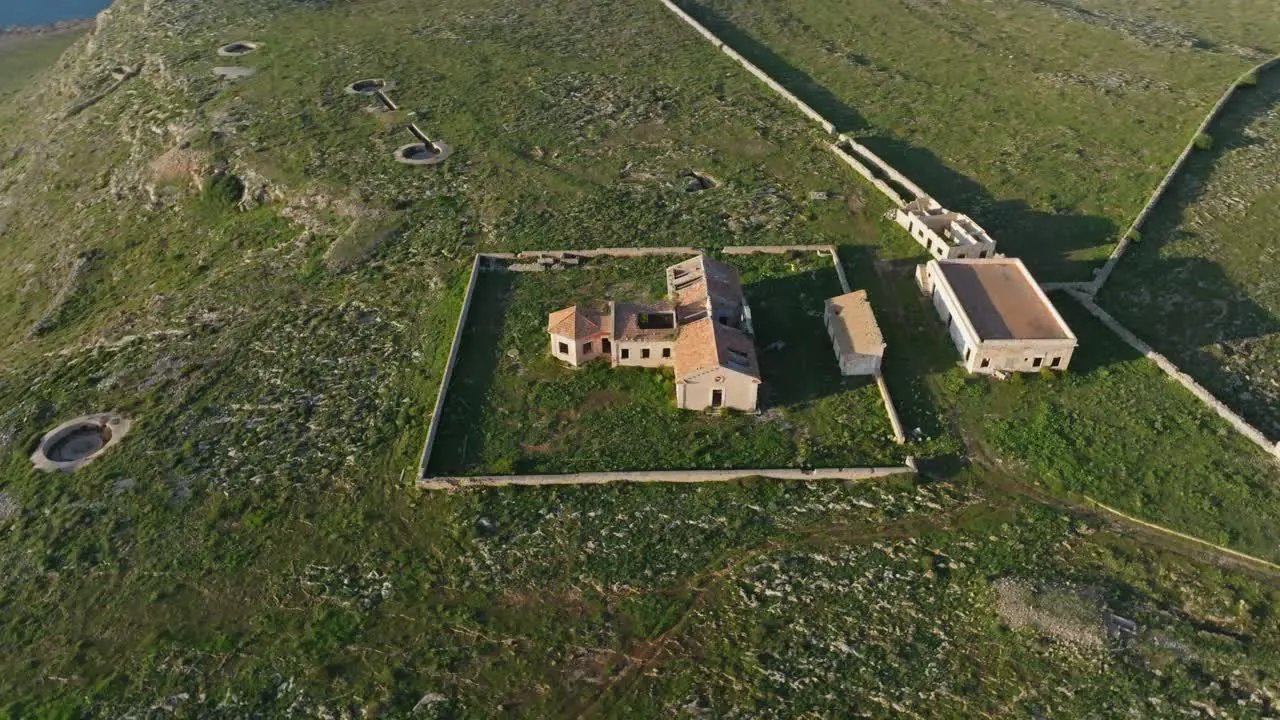 High angle bird's eye view orbits around old decrepit abandoned military building in Minorca Spain