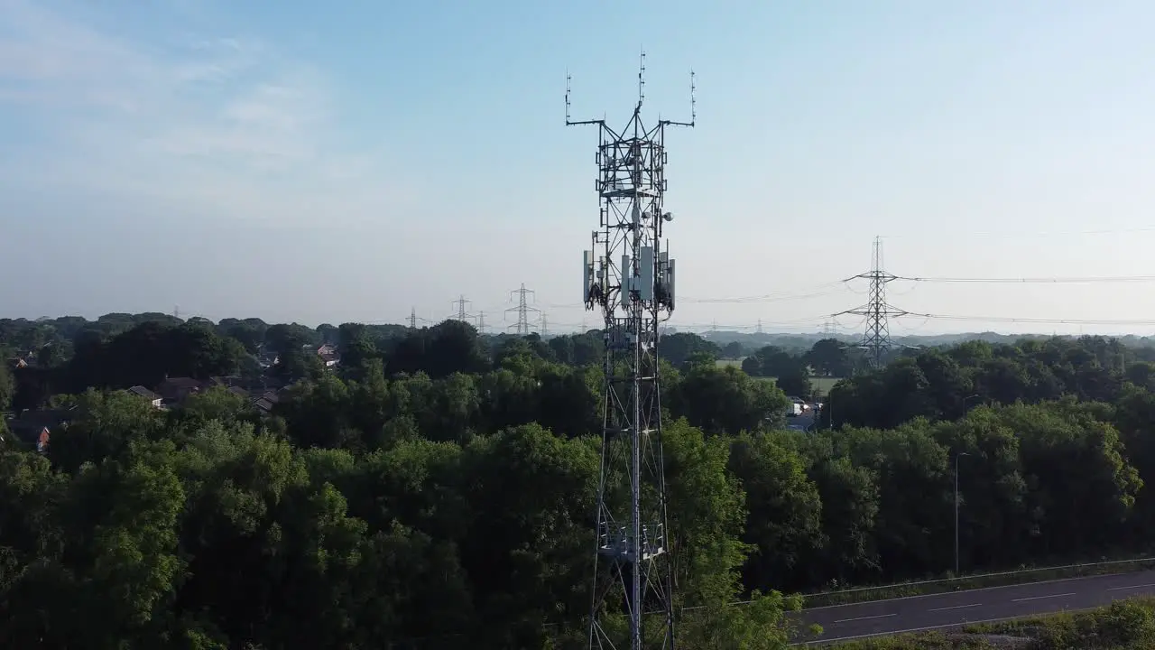 5G broadcasting tower mast in British countryside with vehicles travelling on highway background aerial left orbit view