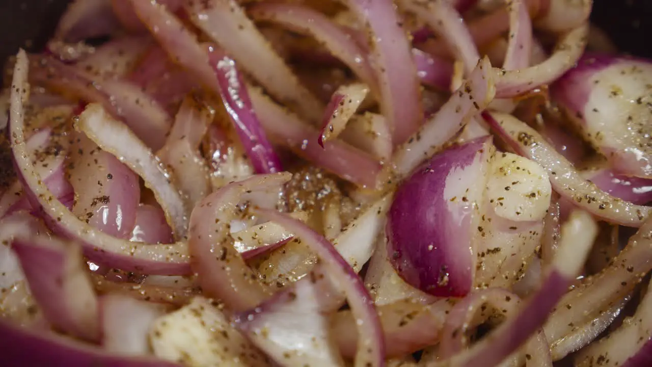 Stirring and shuffling onion slices mixed with spices with a wooden spoon inside cooking pot