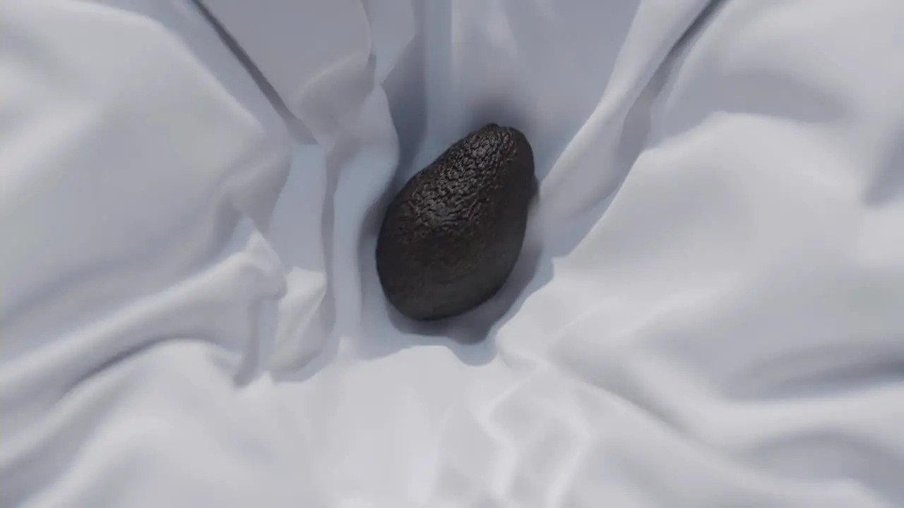 Mesmerizing slow-motion footage of an avocado descending onto a pristine white sheet followed by being carefully enfolded invoking a serene minimalist aesthetic