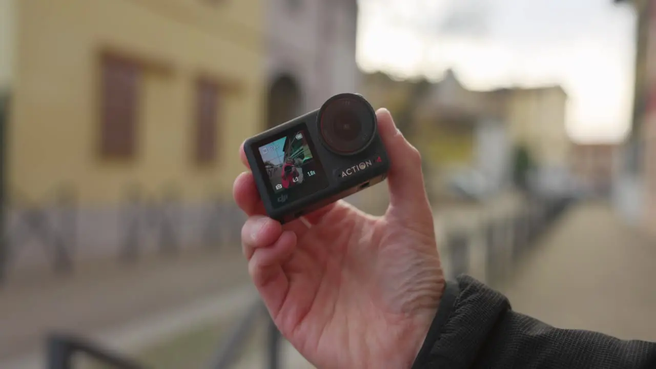 Hand Showcasing DJI Osmo Action Camera Against Blurry Background Outdoor