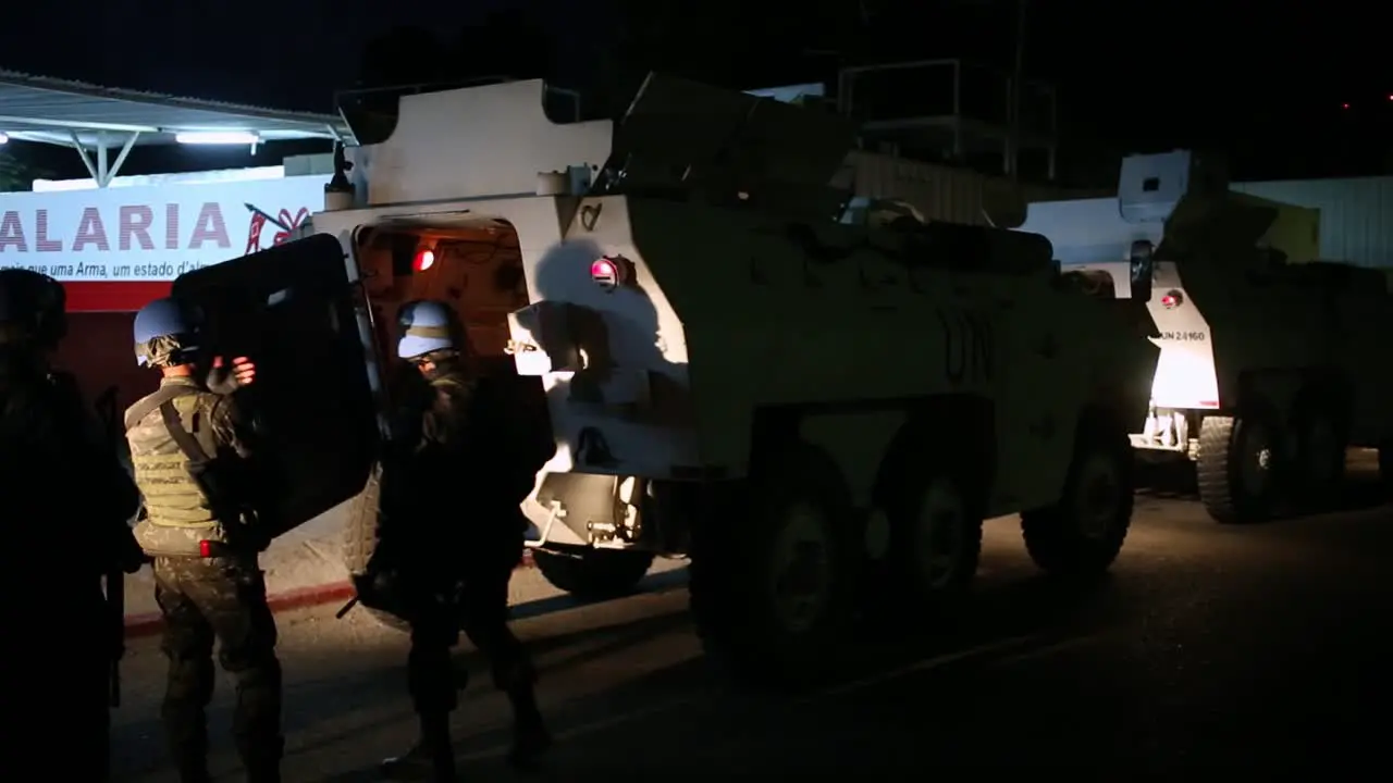 Unit of armed members of the United Nations on a mission next to an armored vehicle on the street at night