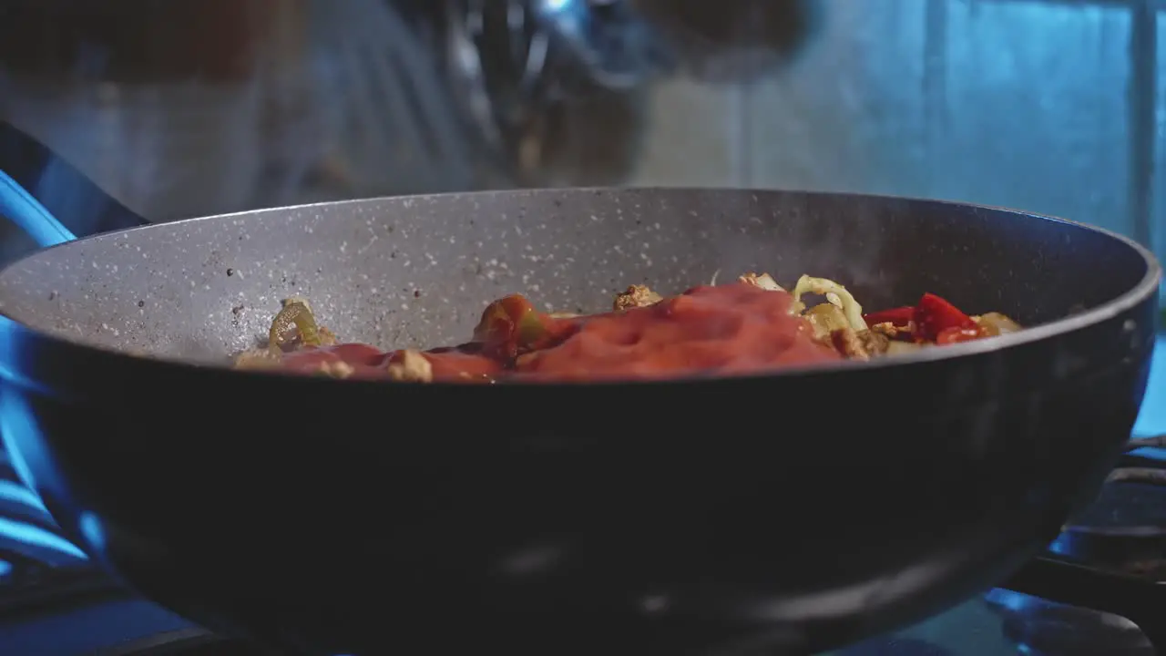 Pouring tomato sauce into a wok with meat and vegetables for mexican tortillas and mixing it all with a wooden spoon