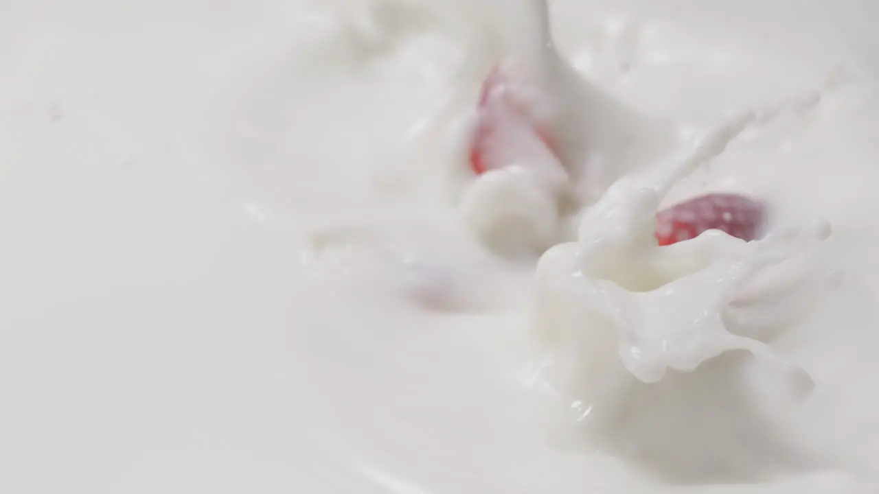 Fresh strawberries falling and dipping in milk