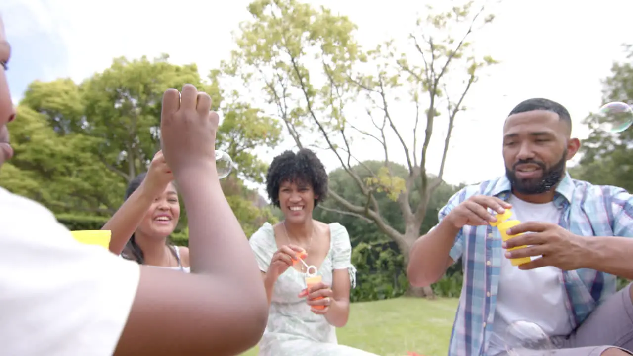 Happy african american parents daughter and son blowing bubbles sitting in garden slow motion