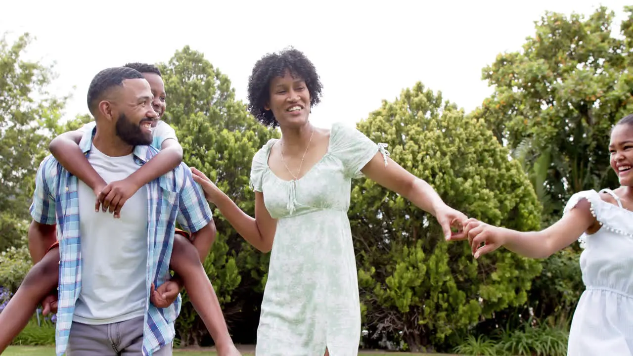 Happy african american parents daughter and son piggybacking and dancing in garden slow motion