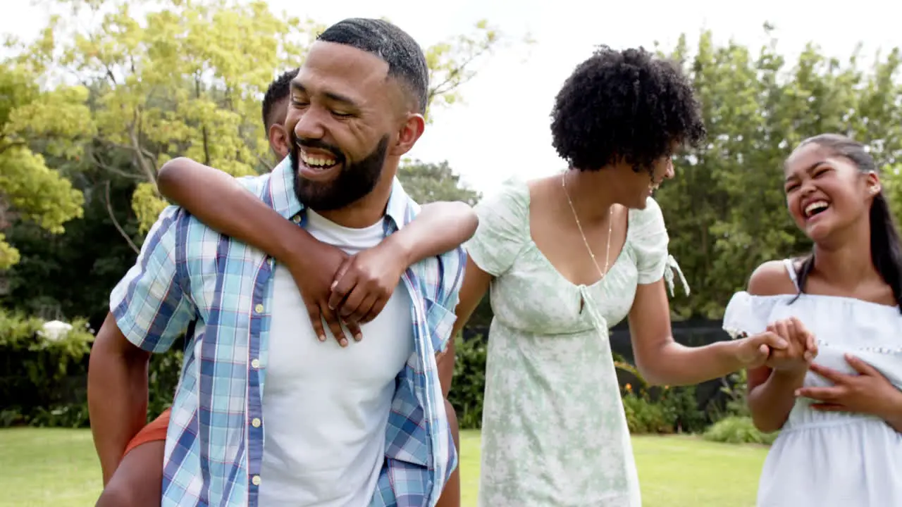 Happy african american parents daughter and son piggybacking and walking in garden slow motion