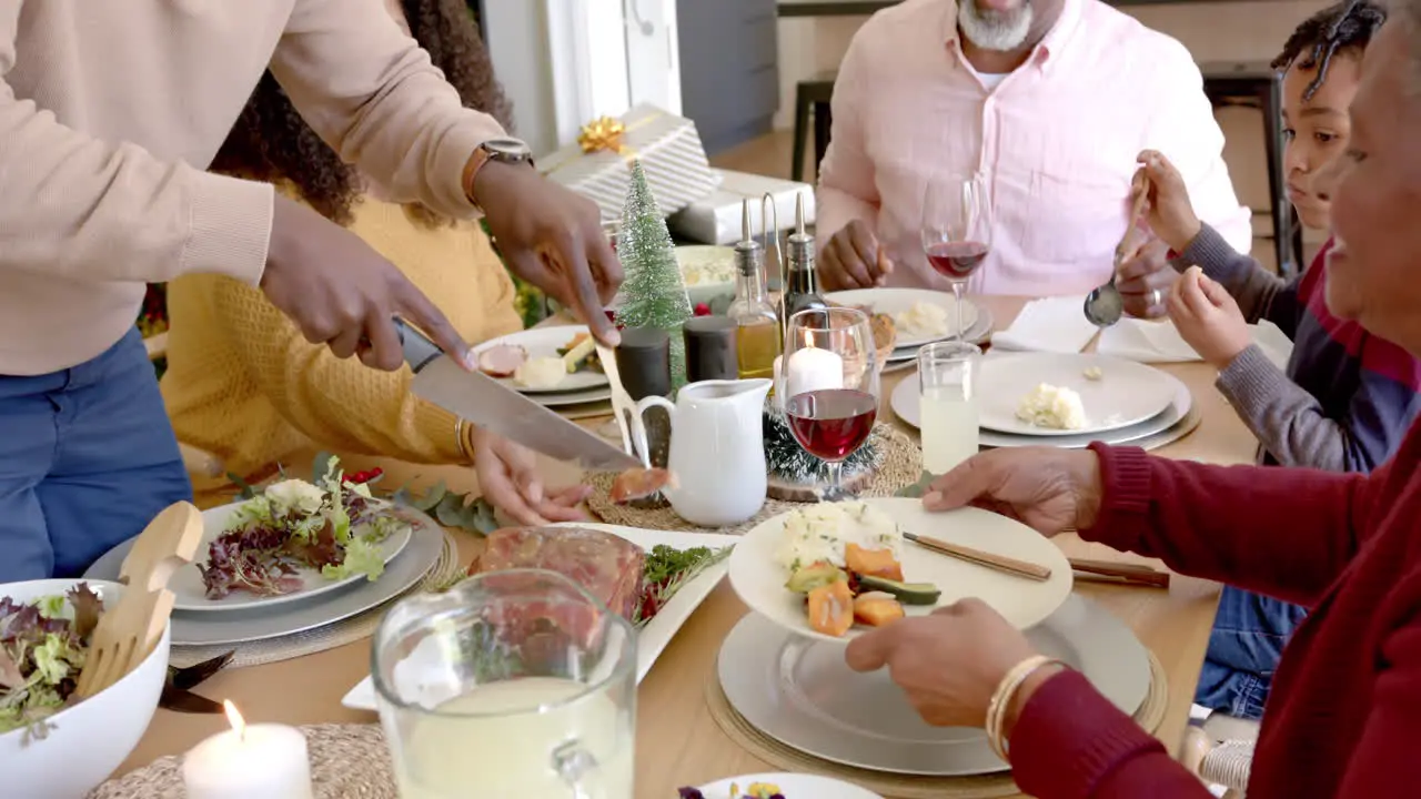 African american father carving meat at multi generation family dinner table