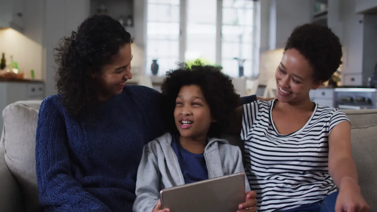 Smiling mixed race lesbian couple and daughter using digital tablet on couch