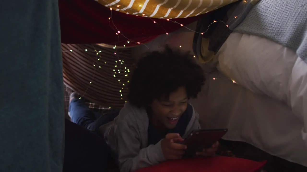 Mixed race girl lying in bedroom fort using digital tablet