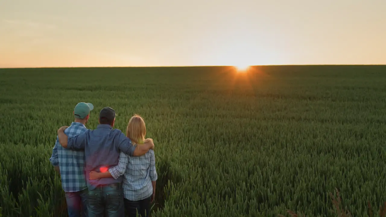 Happy family of farmers admiring the sunset over a field of wheat