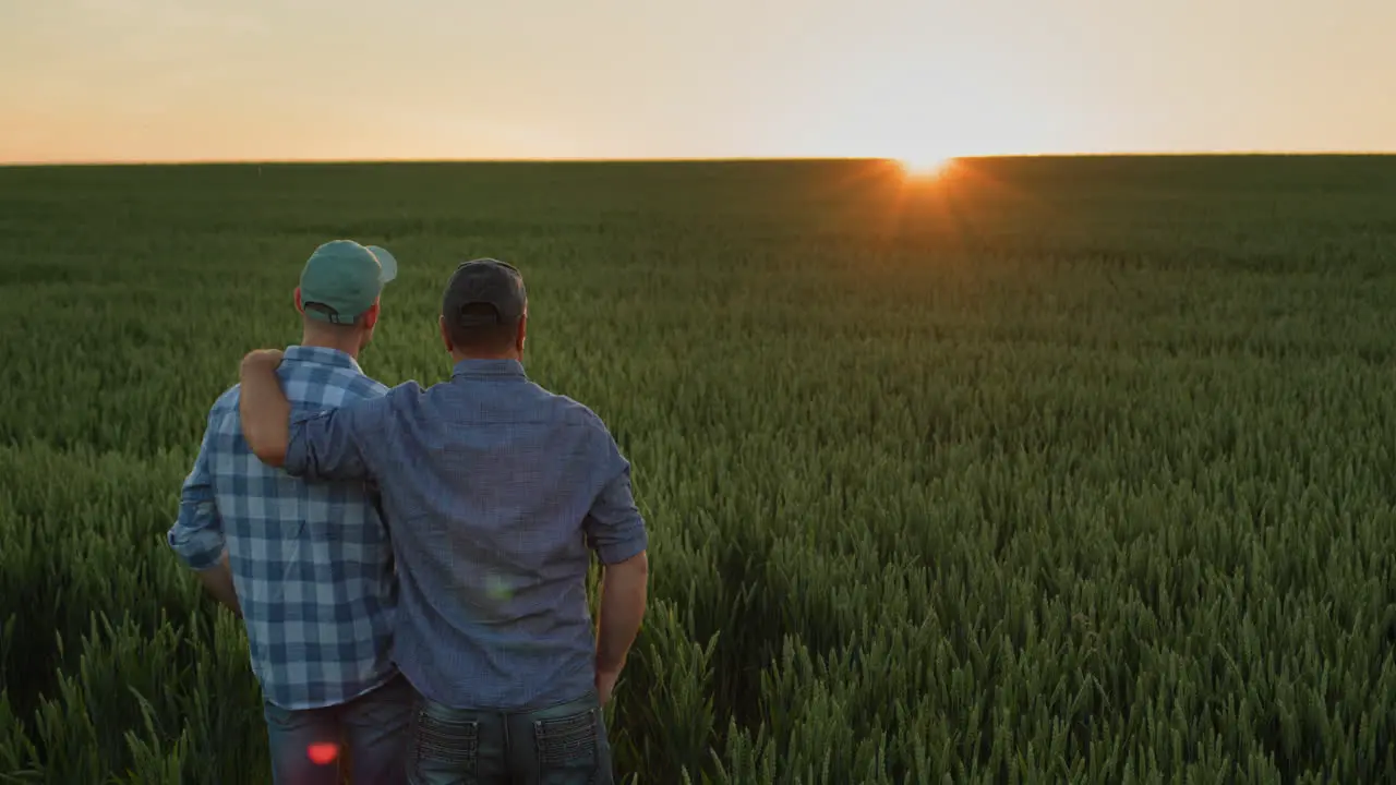 Father farmer hugging his adult son and watching the sunset over the field together