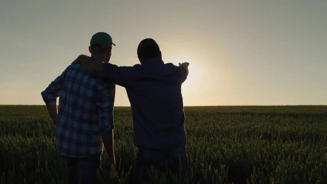 A man and his son watch the sunrise over a wheat field together Farmers in the field and family business