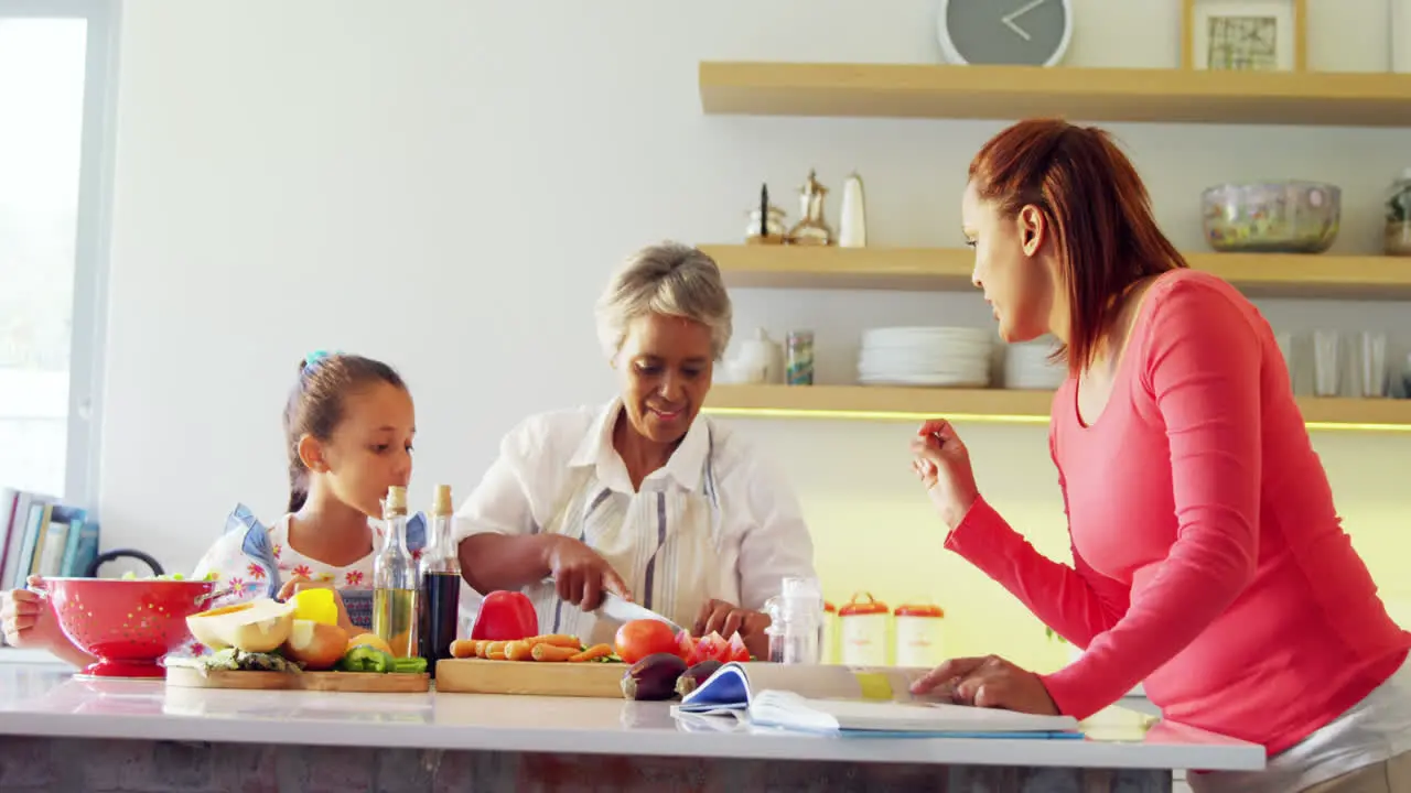 Mother looking recipe book while grandmother and granddaughter chopping vegetables 4k