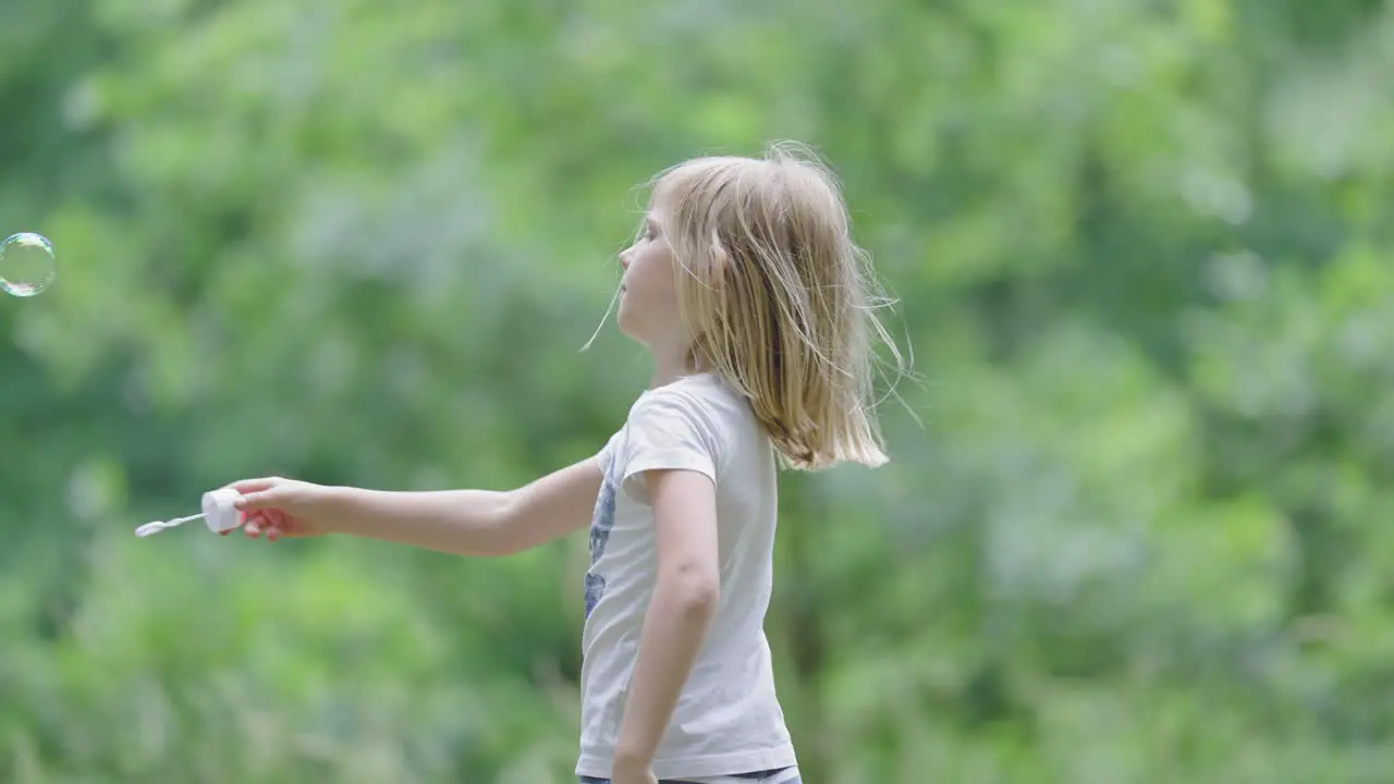 A blonde-haired little girl blowing soap bubbles outside on a sunny day