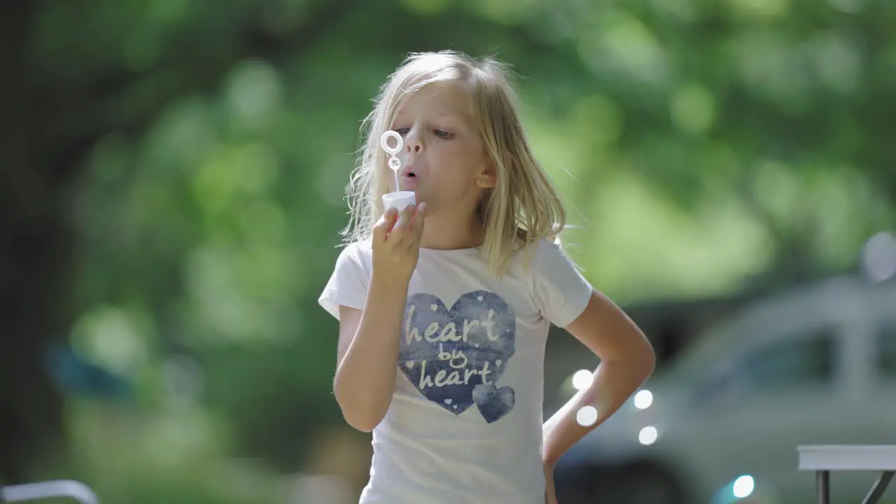 Little girl with blonde hair plays with soap bubbles outdoors