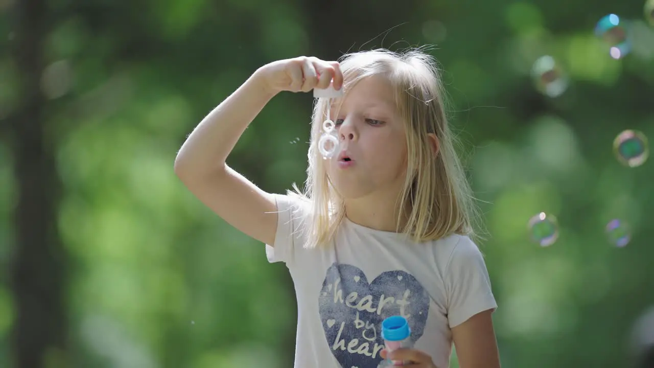 A cheerful young blonde girl immerses herself in outdoor play creating soap bubbles that dance in the sunlight