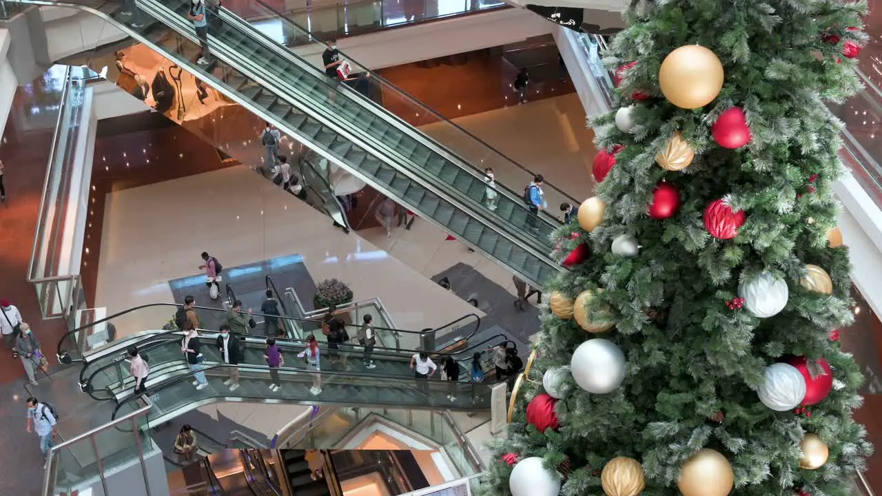 Shoppers ride on escalators at a shopping mall as a Christmas tree installation is seen in the foreground