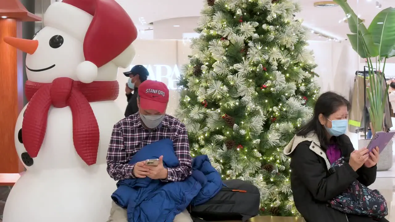 Shoppers sit on a bench next to a Christmas tree and snowman installation at a shopping mall in Hong Kong