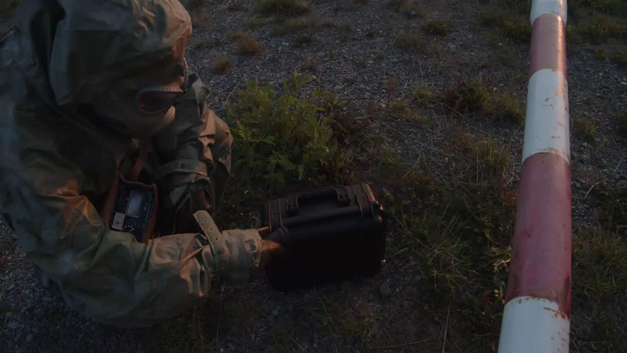 Soldier in a protective suit checks the radiation of a suspicious briefcase at the barrier