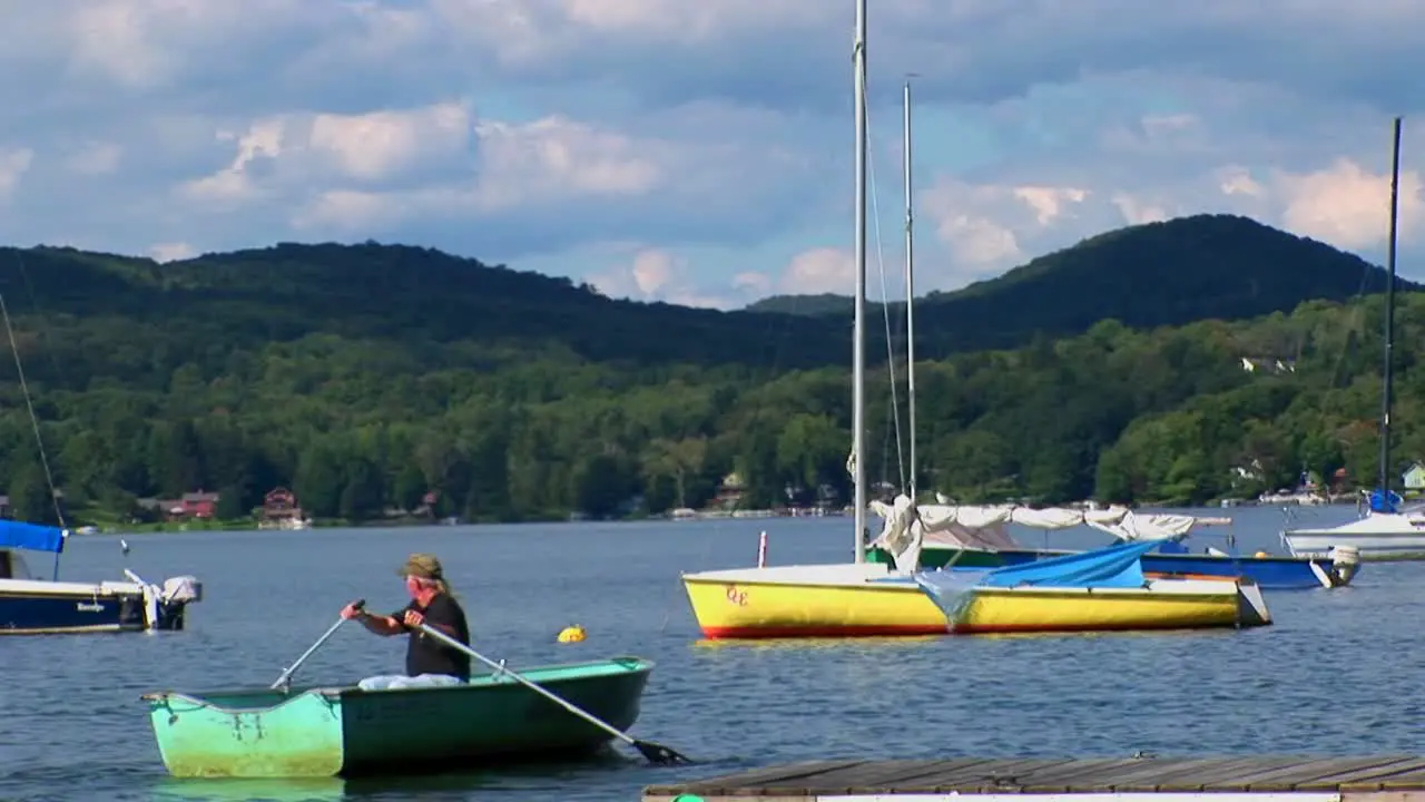 A man drifts in a rowboat near sailboats and a dock on a rural lake in Central Vermont 