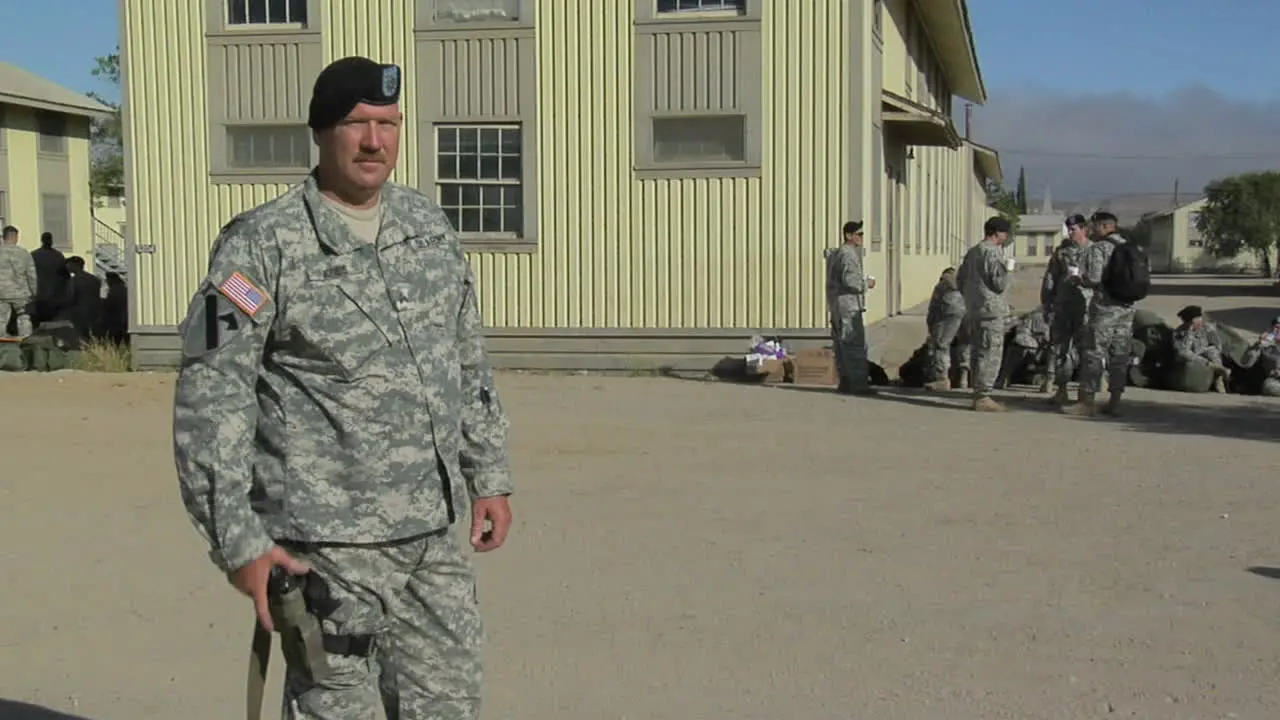 A soldier draws a hand gun then points to a patch on his arm