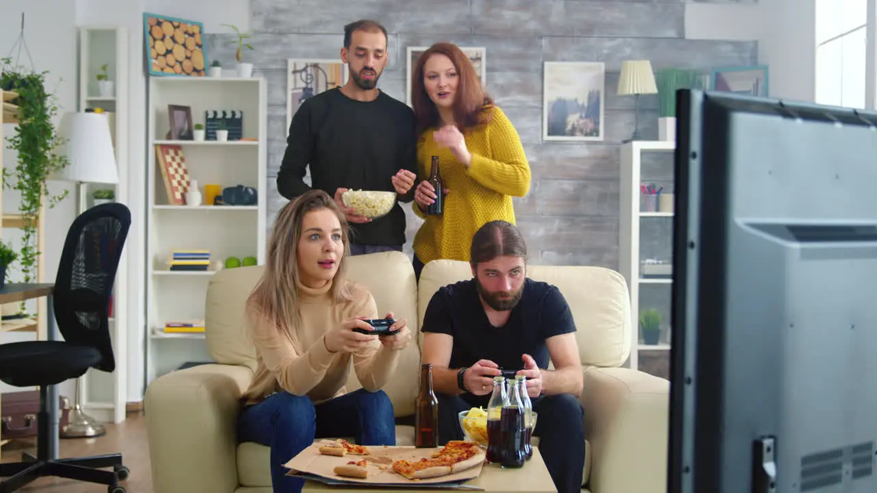 Young couple eating popcorn while their friends are playing video games